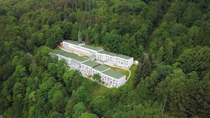 En modern, flervåningsbyggnad med ett platt tak, omgiven av tät skog.