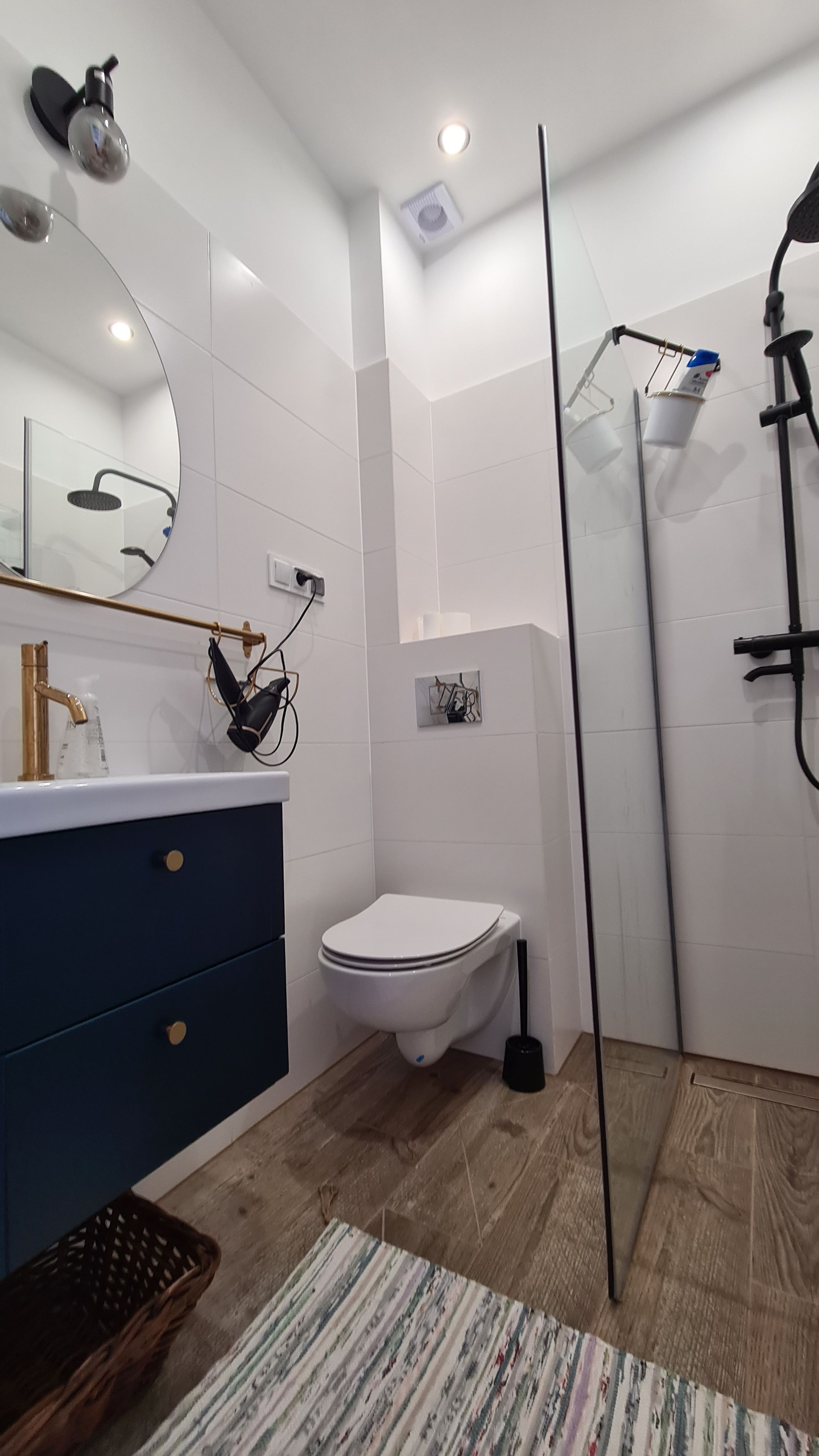 Ein modernes Badezimmer mit Toilette in Weiß, einem Waschbecken mit goldener Armatur, einem Spiegel und einer Duschkabine.