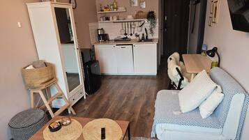 Un espacio habitable compacto con kitchenette, un sofá, una mesa de comedor y una pequeña mesita auxiliar.