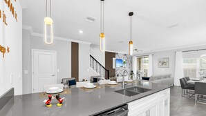 A modern kitchen with a large island, stainless steel appliances, pendant lighting, and a dining area with a gray sofa and table.