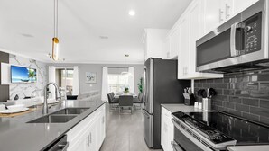 A modern kitchen with stainless steel appliances, a marble backsplash, and a dining area with a view of the outdoors.