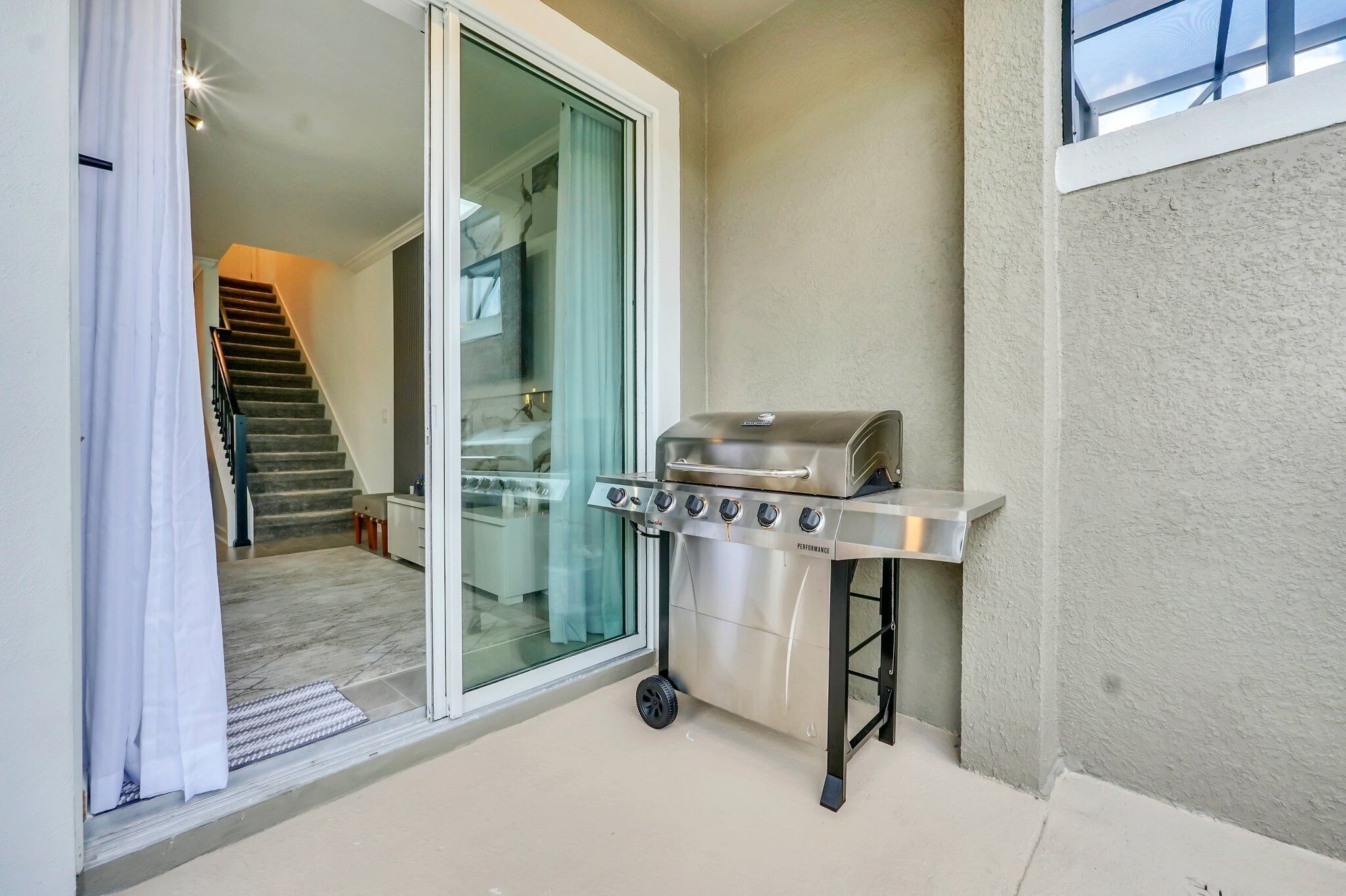 A balcony with a sliding glass door leading to a staircase, a portable stainless steel grill, and a small table.