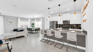 A modern kitchen with a central island, bar stools, and pendant lighting.