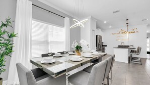 A modern dining area with a long table set for four, a kitchen in the background, and a wall with a Disney Dream quote.