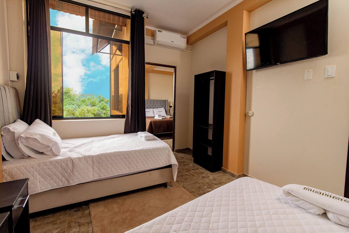 A hotel room with two beds, a TV mounted on the wall, and a window with curtains.