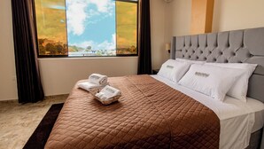 A hotel room with a large window, a bed with a brown quilt, white pillows, and a grey headboard. - SONQU TARAPOTO HOTEL  (Tarapoto)