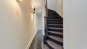 A staircase with a wooden handrail and black steps, leading to a landing with a white wall and a light fixture.