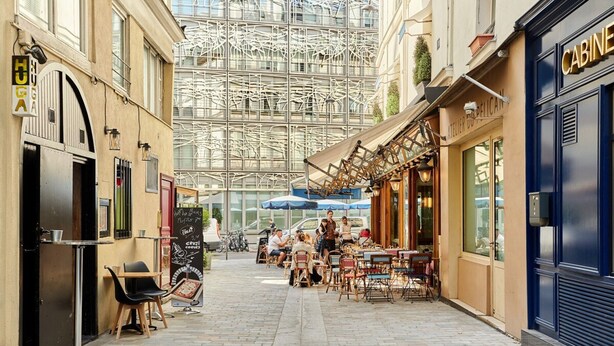 A narrow street with outdoor seating, a café, and a blue storefront.