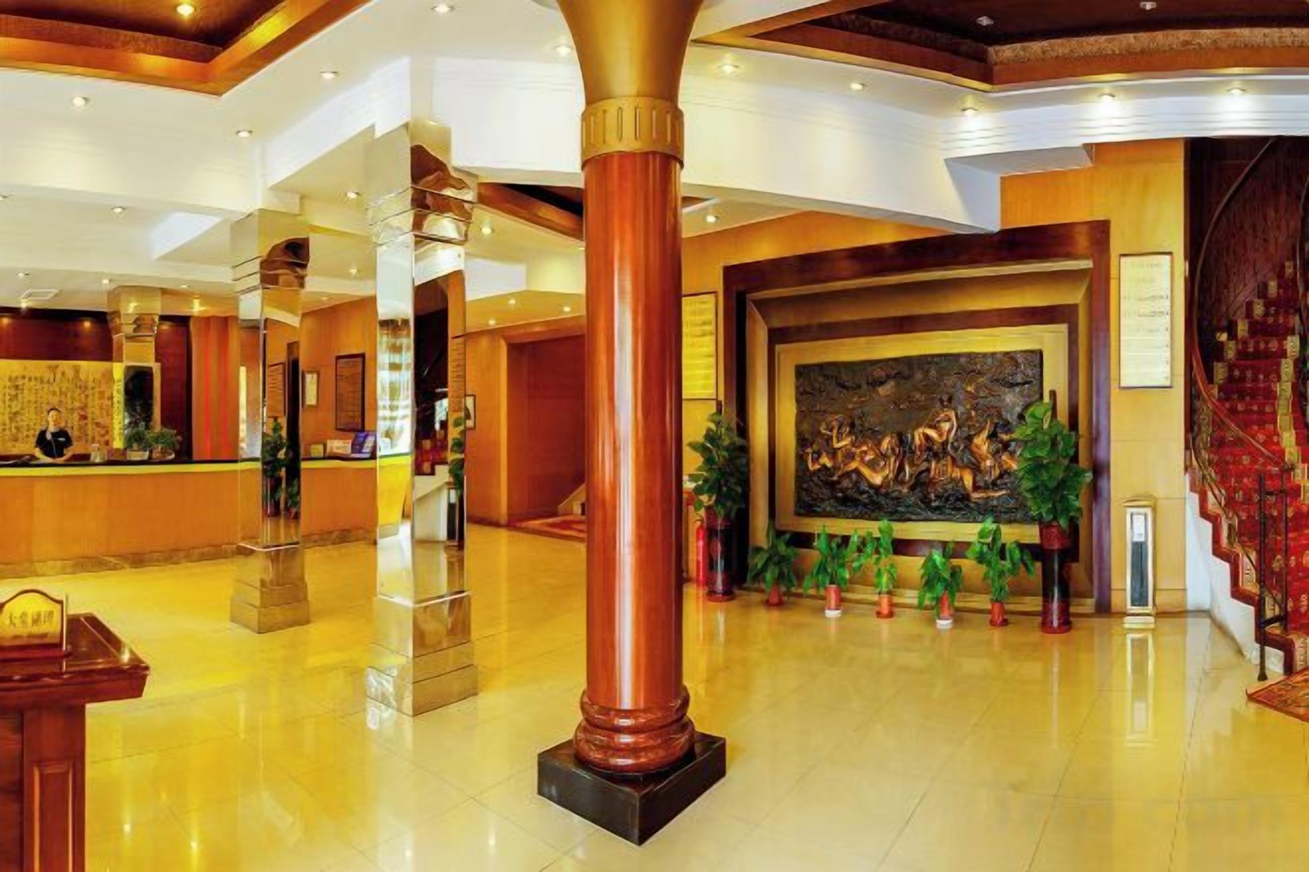 A hotel lobby with a reception desk, a large painting, and a staircase.
