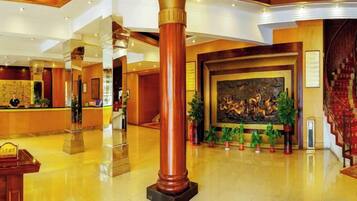 A hotel lobby with a reception desk, a large painting, and a staircase.