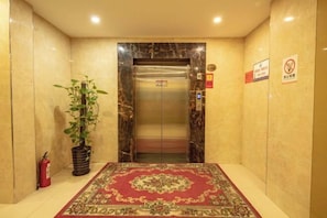 An elevator with a marble finish, a red patterned carpet, and a potted plant. - Zhezhi Jianguo Hotel (Lu Xun's hometown) (Shaoxing)