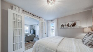 A bedroom with a large bed, a chandelier, and a view of the outside. - Charming Downtown Retreat for Weddings, Weekends & Outdoor Fun! (Delano)