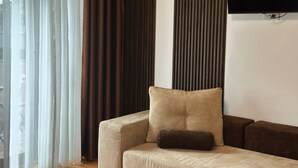 A modern living room with a beige sofa, a dark brown cushion, and a flat-screen TV mounted on the wall. - Hillside Garden (Skopje)