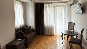 A modern living room with a sofa, a small table with chess, and a TV mounted on the wall. - Hillside Garden (Skopje)