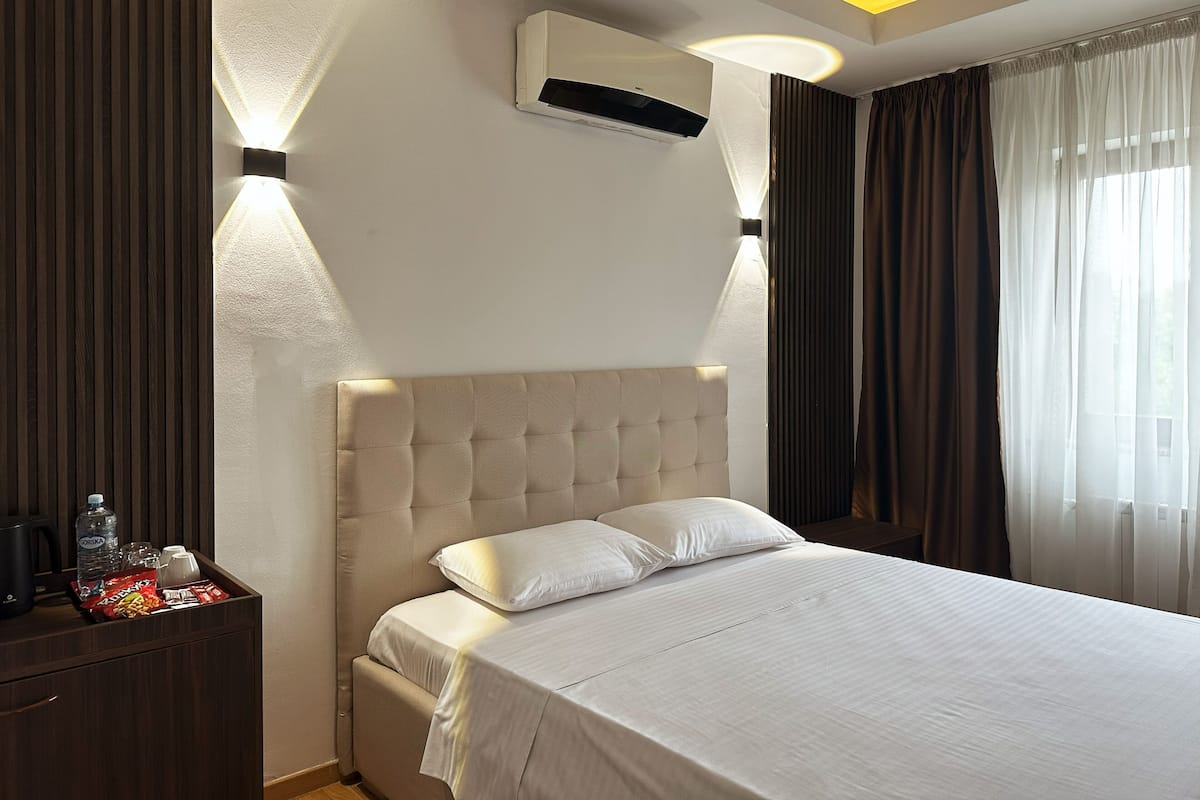 Ein Hotelzimmer mit Bett, Nachttisch, Klimaanlage und Vorhängen.
