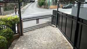 A stone-paved entrance with a metal gate, a covered walkway, and a view of the street. - Hillside Garden (Skopje)