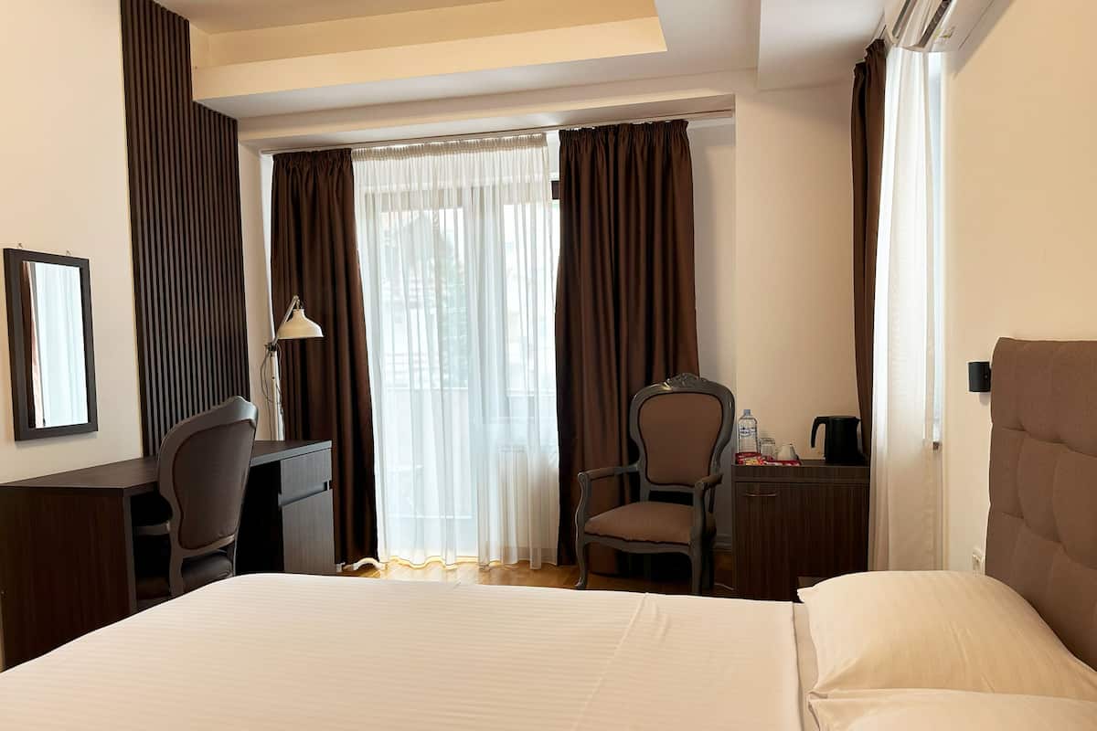 Ein Hotelzimmer mit Bett, Schreibtisch, Stuhl, Lampe und einem Fenster mit Vorhängen.