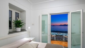 Un dormitorio con cama, planta en maceta, ventana y balcón con vista al mar.