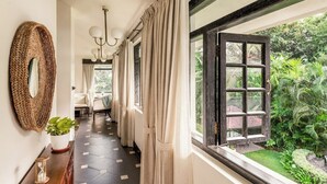 A hallway with a geometric patterned floor, a large mirror, a potted plant, a wooden console table, and a window with curtains. - Viraam Estate by RÊVE/Infinity heated pool with caretaker/Chef (Assagao)