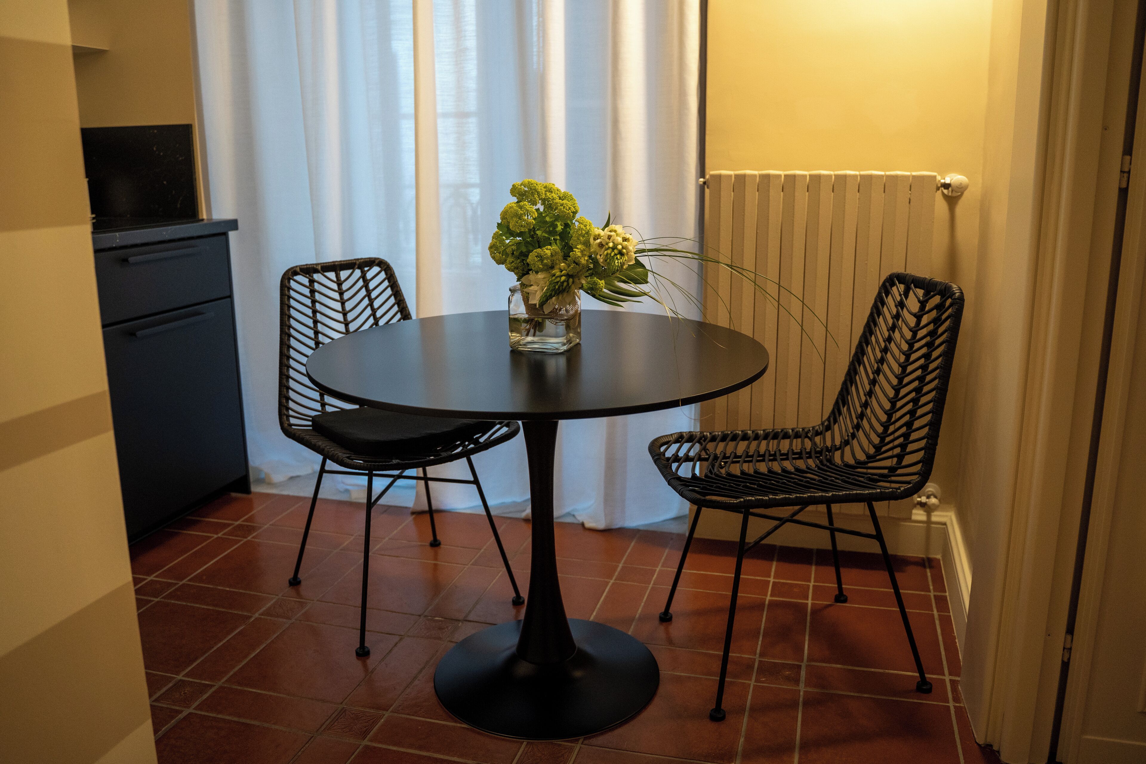 Un pequeño comedor con una mesa redonda, dos sillas y un jarrón con flores.