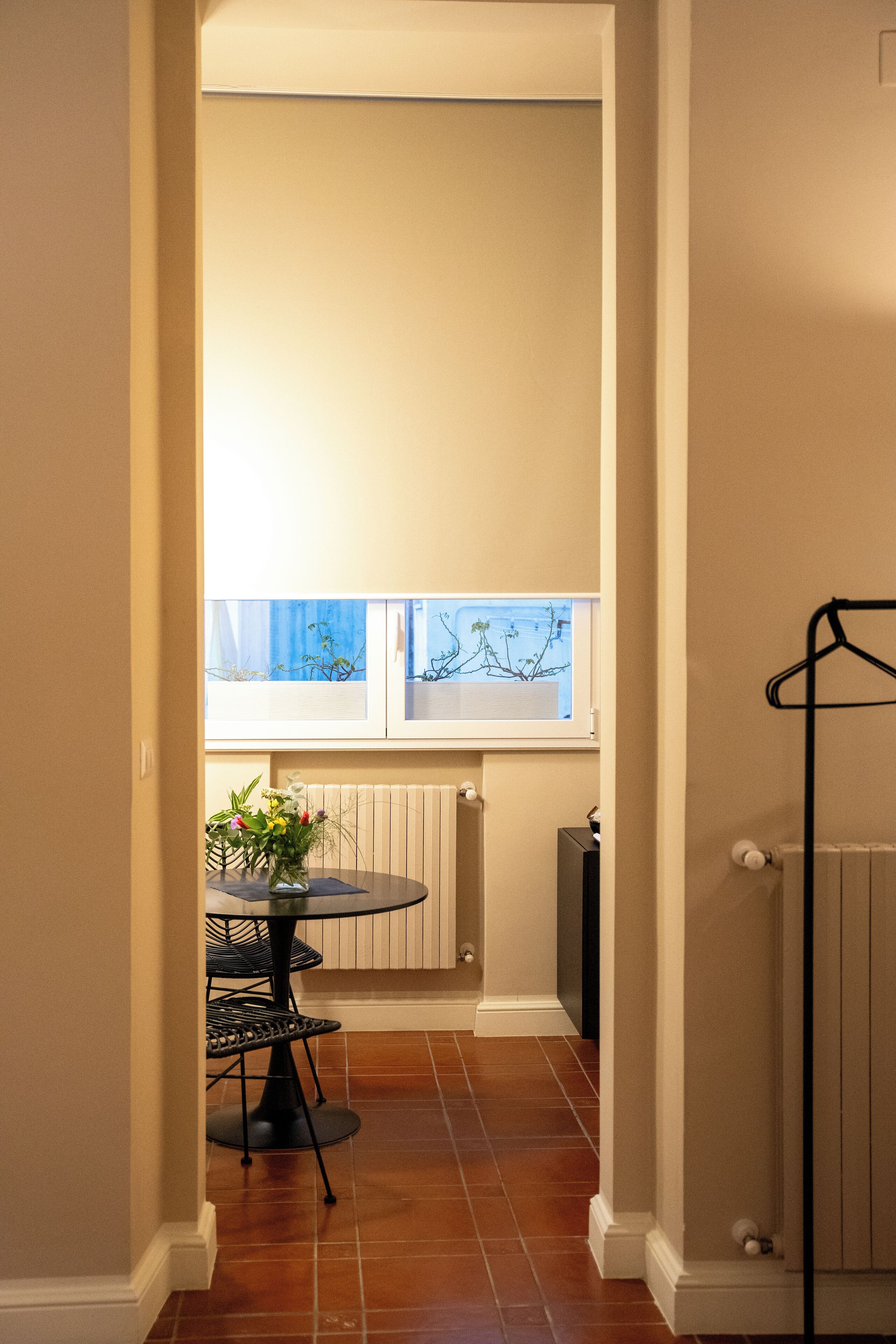 A narrow hallway with a dining table and chairs, a radiator, and a window with a view of the outside.