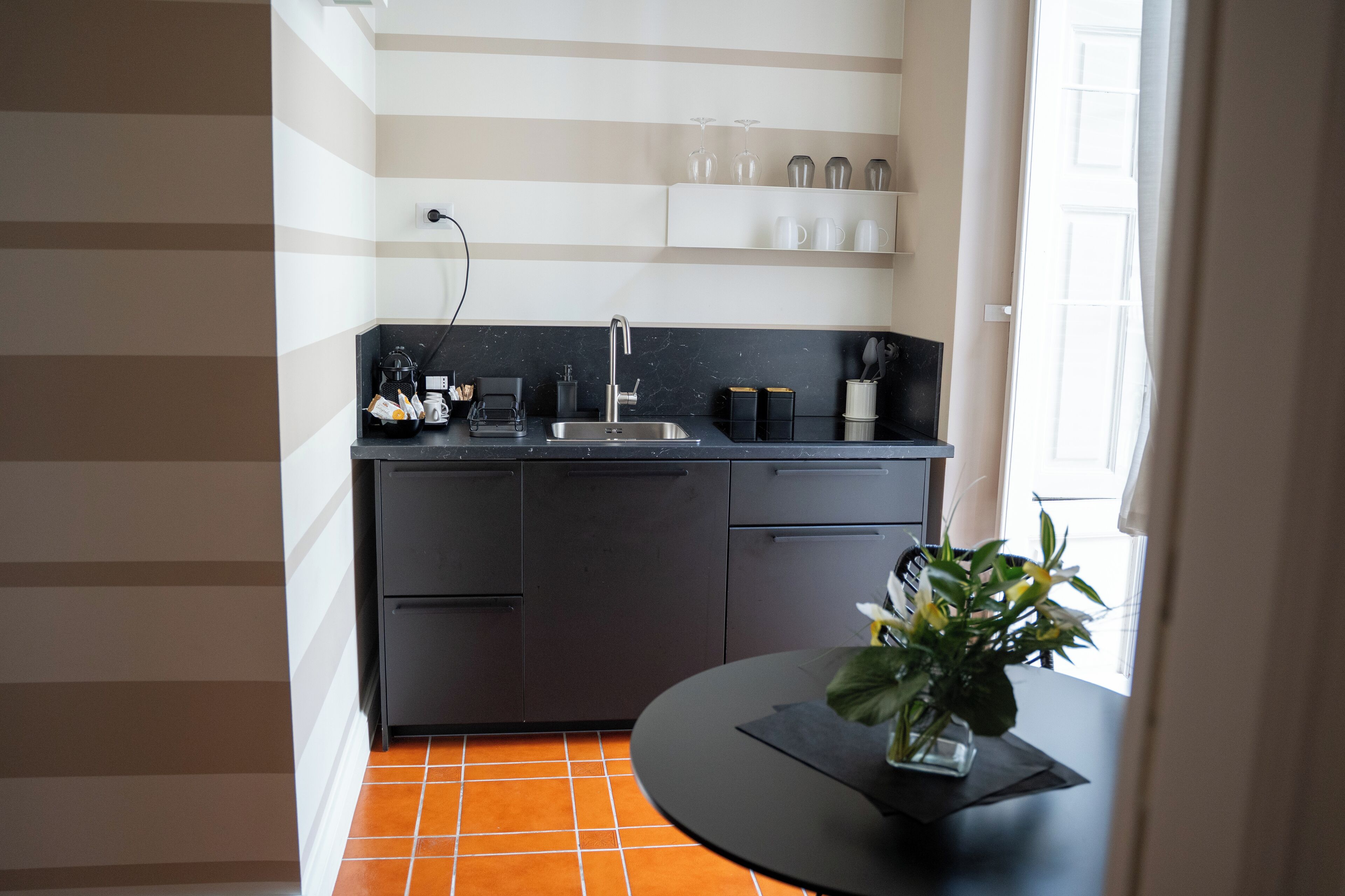 A modern kitchen with a black countertop, a sink, and a dining area with a table and a potted plant.