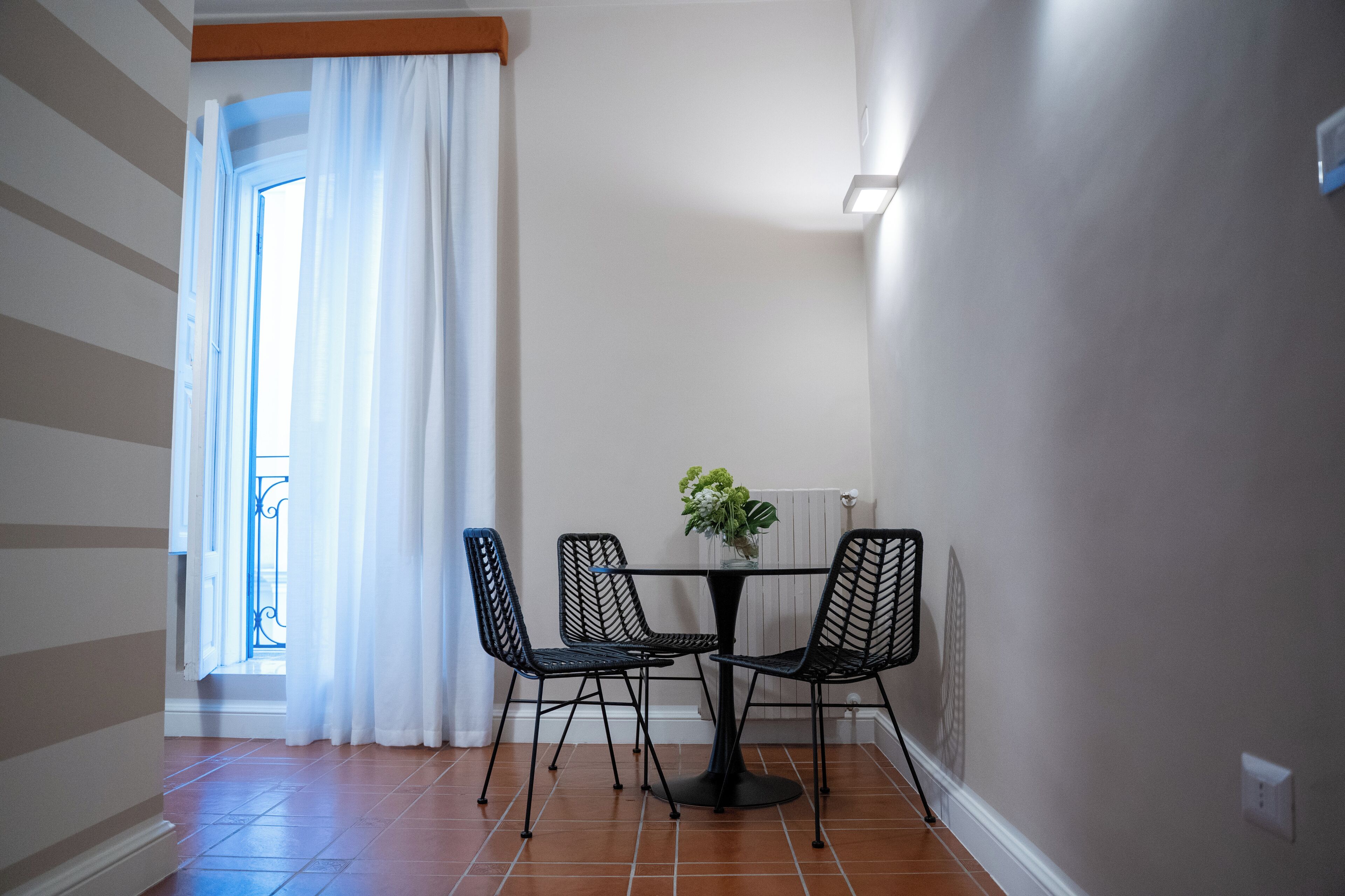 Ein Zimmer mit Esstisch und Stühlen, einem Fenster mit Vorhängen und einem Heizkörper.