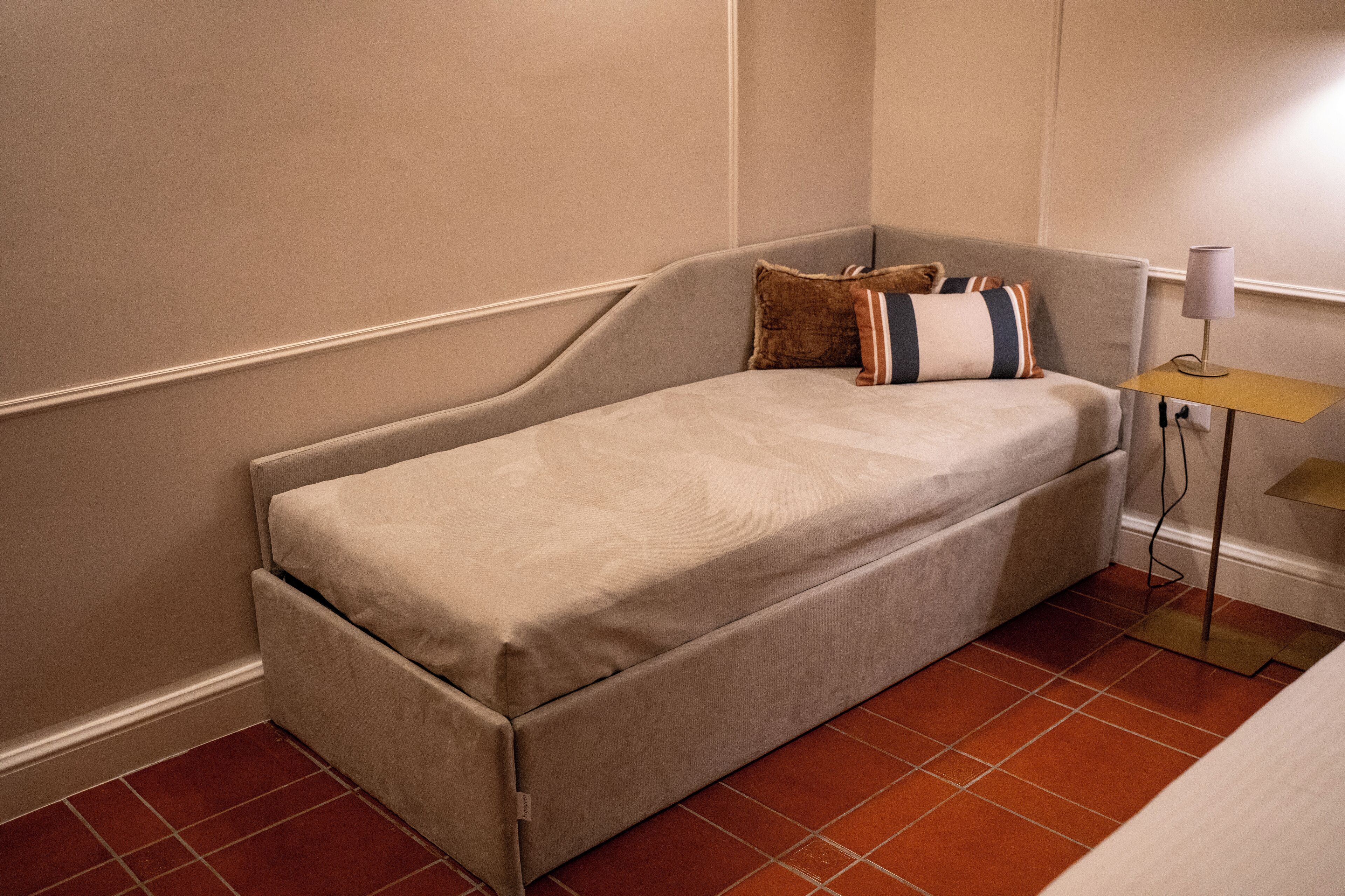 Una stanza piccola con un letto singolo e un divano letto pieghevole, un comodino e una lampada.