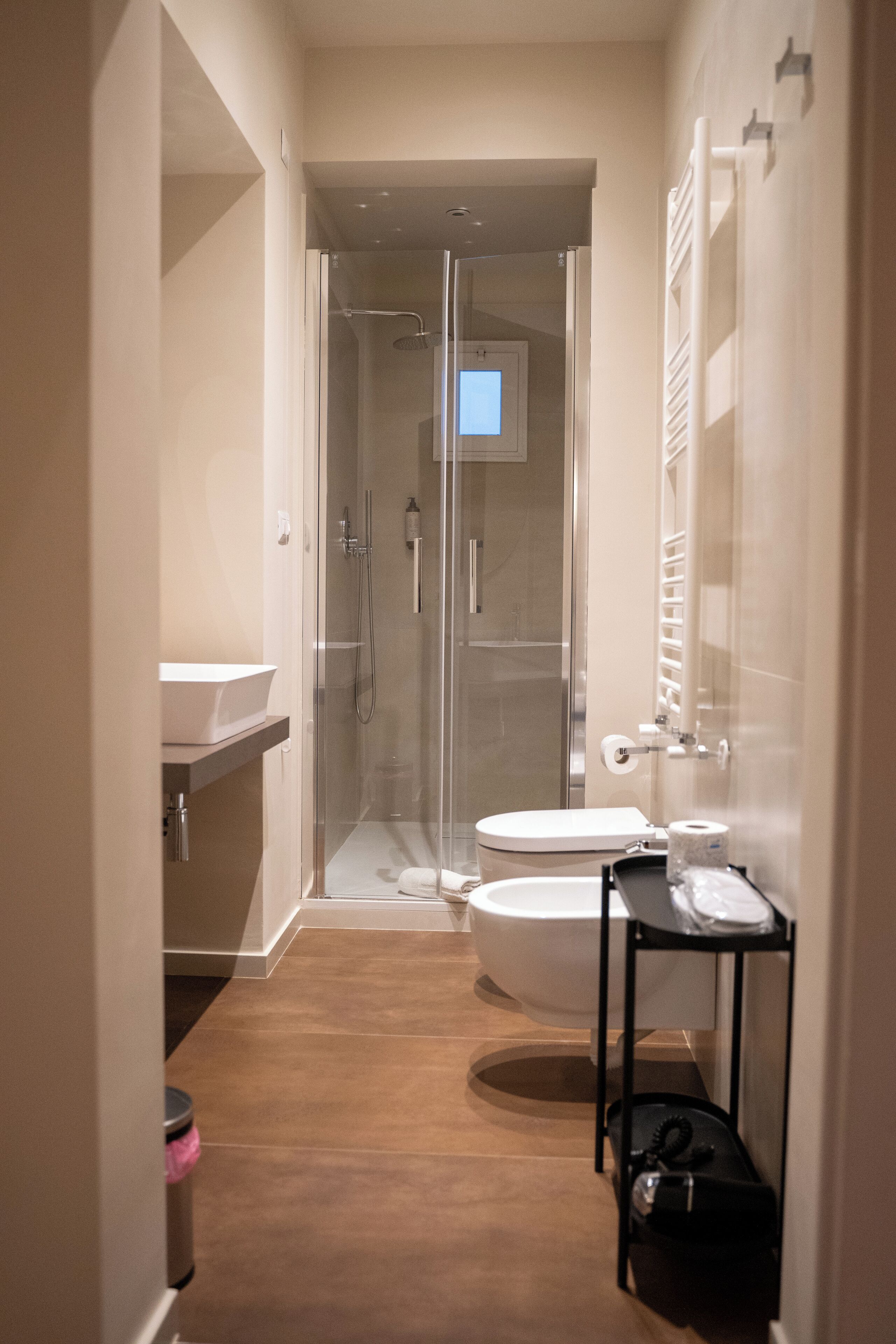 Un baño moderno con ducha de vidrio, inodoro blanco y un lavamanos pequeño.
