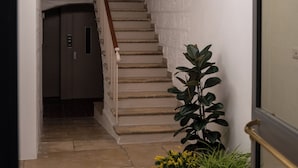 Un escalier surmonté d’un luminaire aux formes géométriques, une plante en pot et une porte donnant sur une pièce.