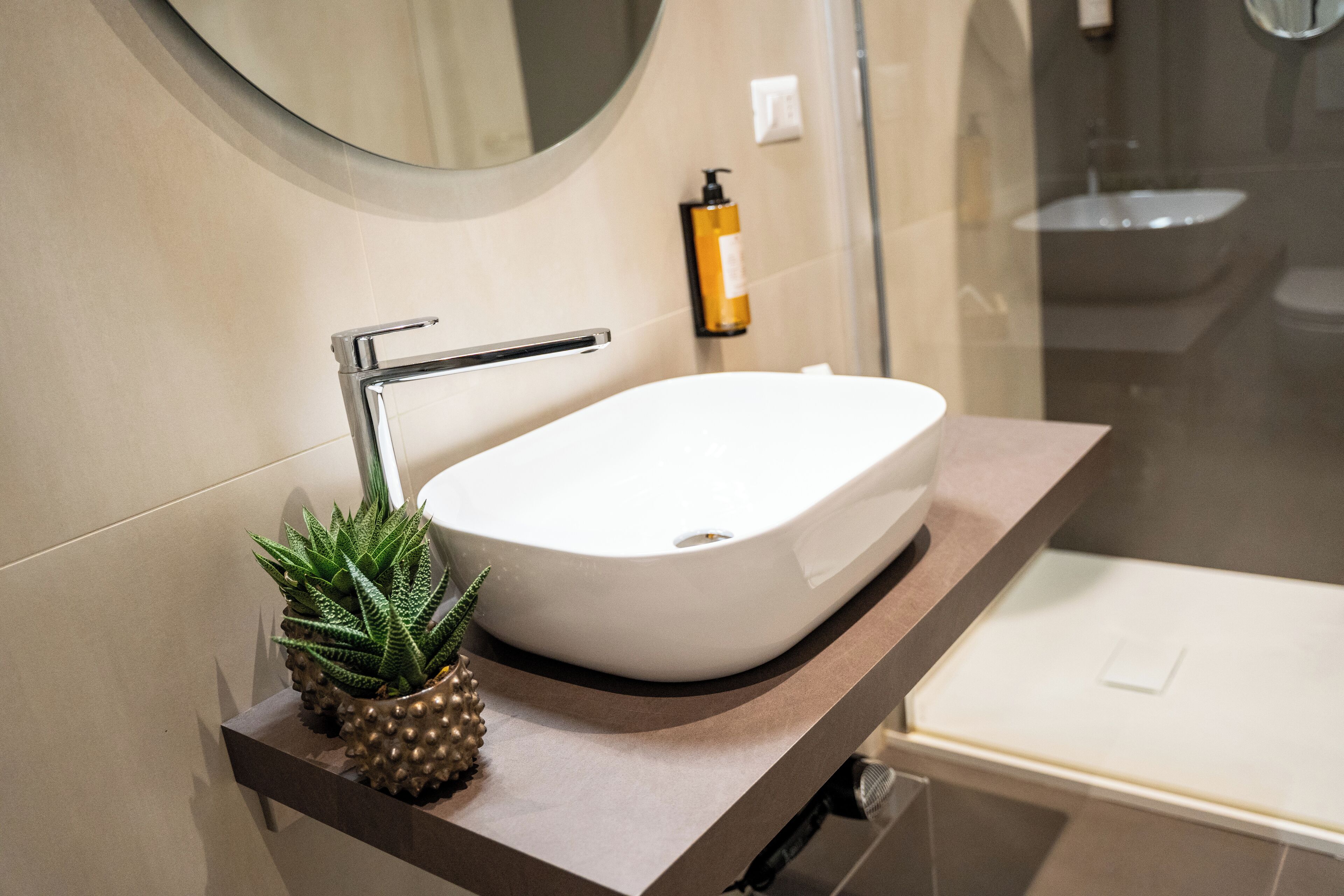 Une salle de bain avec un lavabo blanc, un miroir rond et une petite plante en pot.
