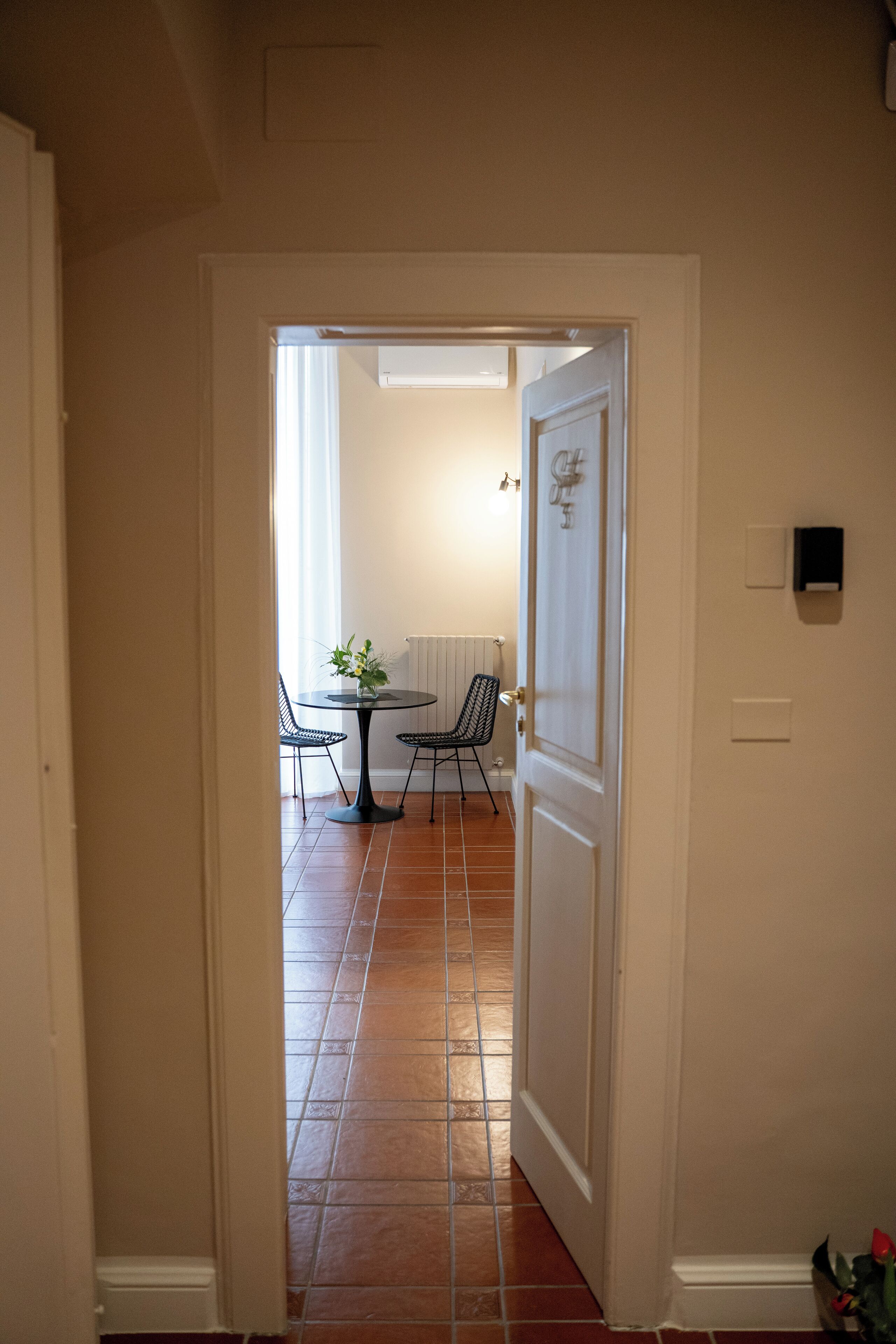 A hallway leading to a dining area with a table and chairs, a radiator, and a door with a light switch.