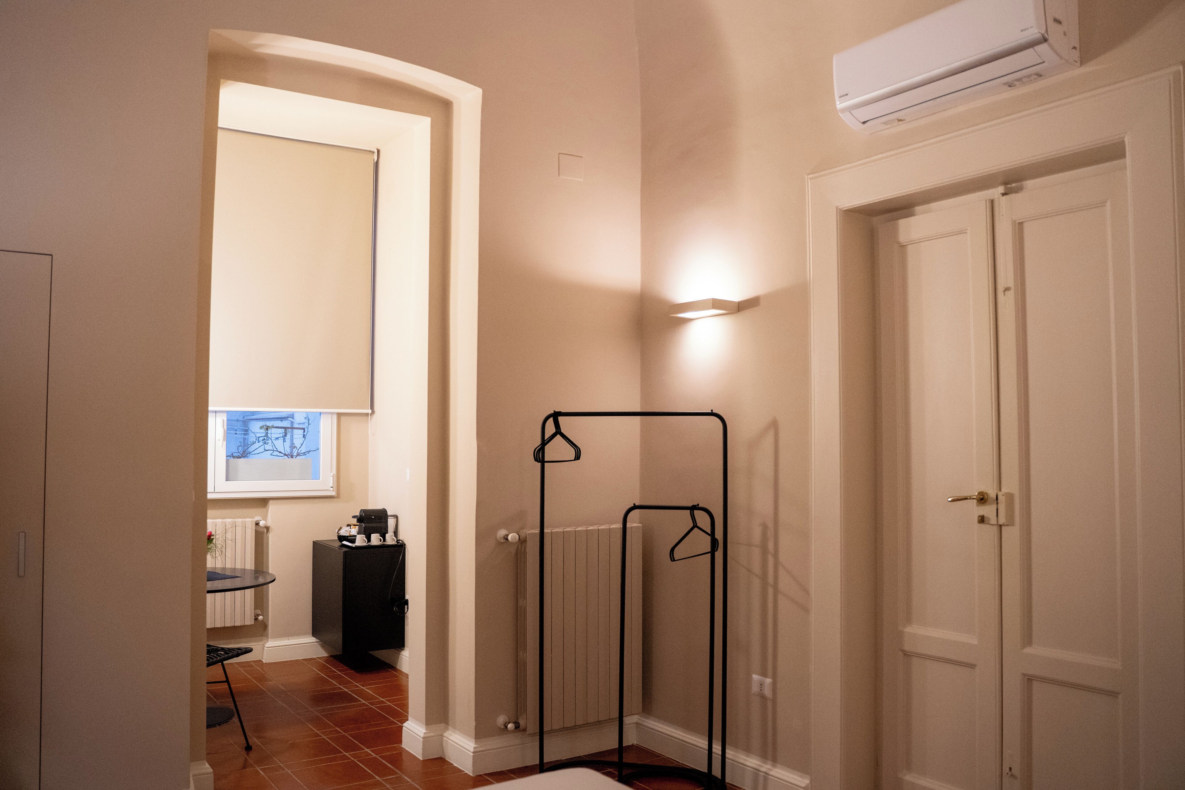 A hallway with a radiator, a radiator cover, a black stand, and a white door.