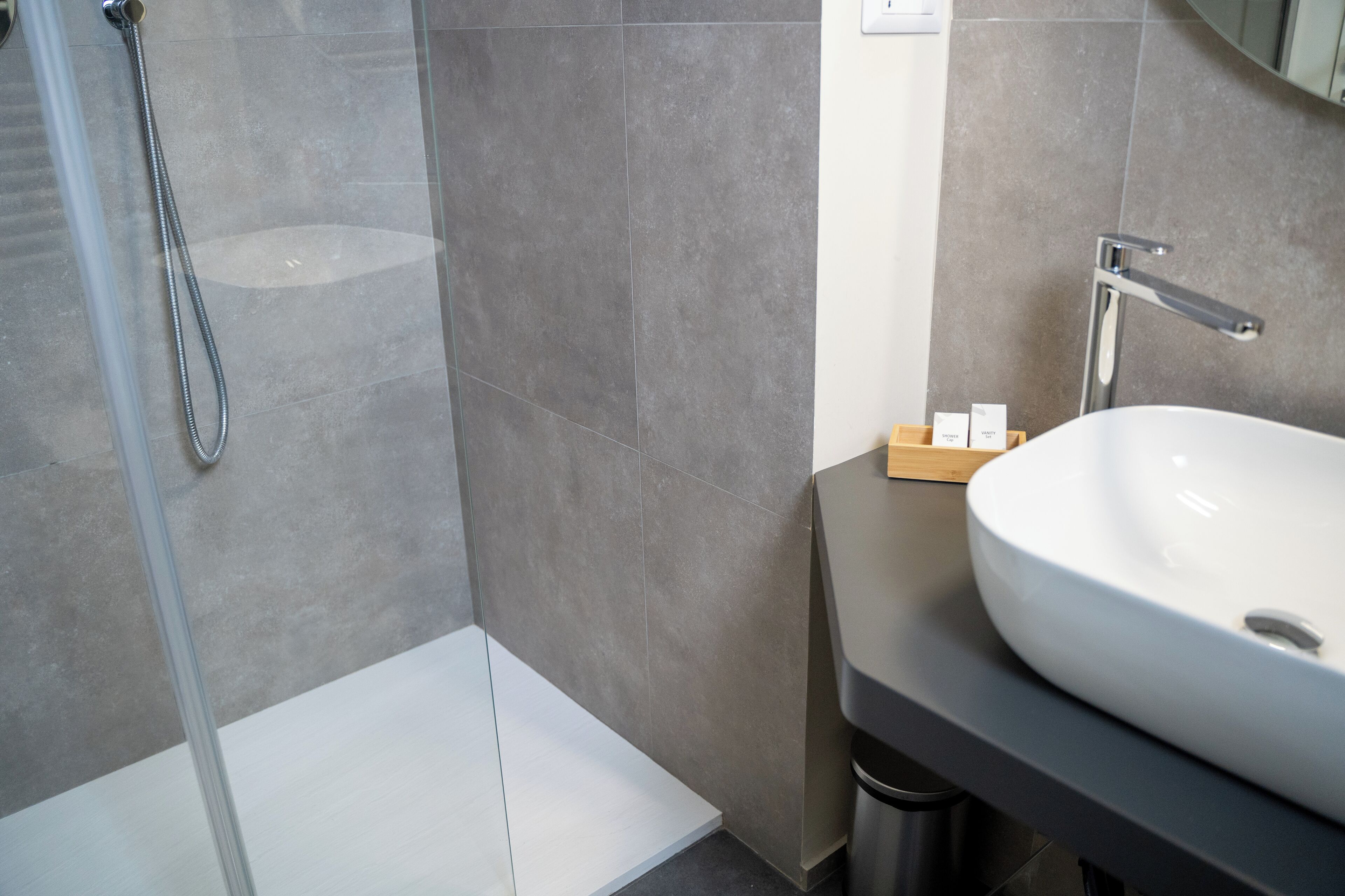 A modern bathroom with a large white sink, a shower with a glass door, and a small wooden box on the countertop.