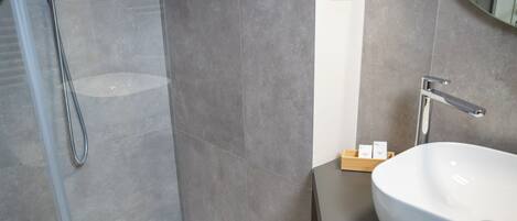 A modern bathroom with a large white sink, a shower with a glass door, and a small wooden box on the countertop.