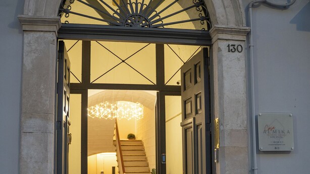 L’entrée d’un hôtel, avec une grande porte en arc de cercle, un escalier menant à l’intérieur et une enseigne indiquant le nom de l’établissement.