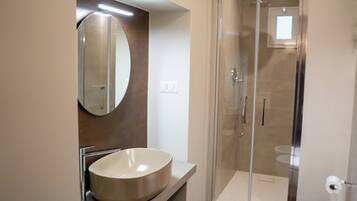A modern bathroom with a large oval sink, a mirror, and a glass-enclosed shower.