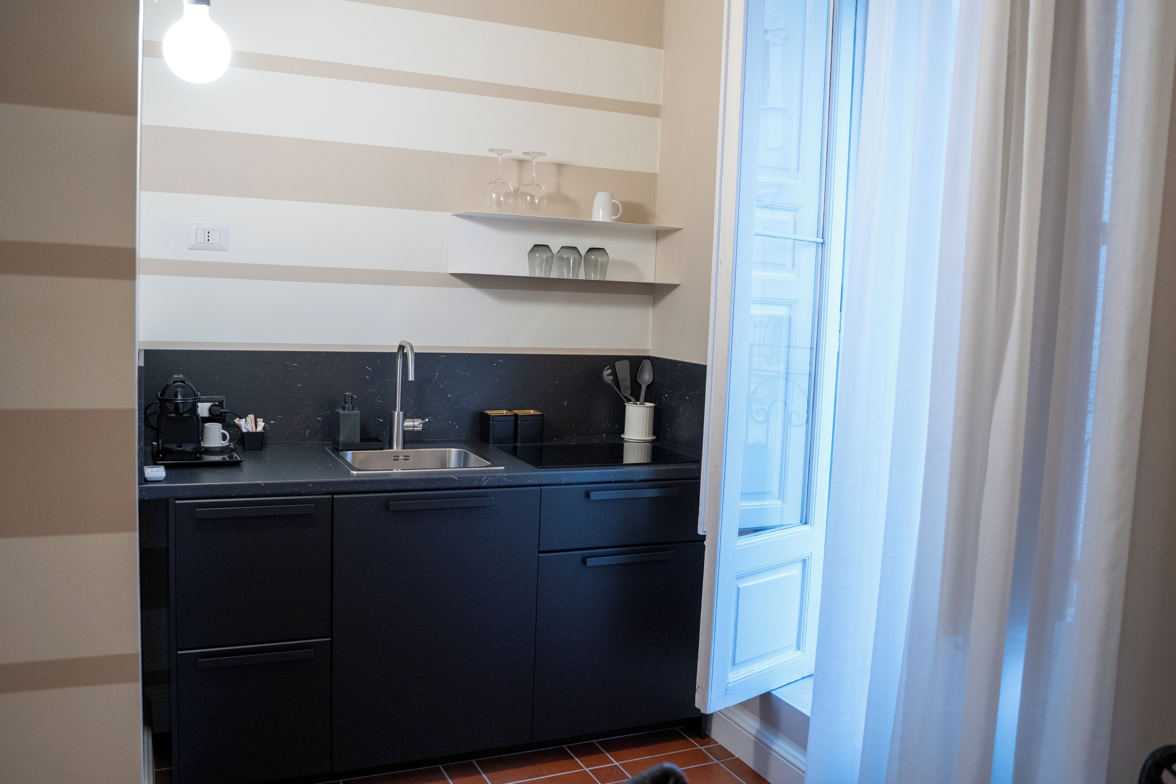 Una cocina con armarios negros, un lavamanos y una ventana con cortinas.