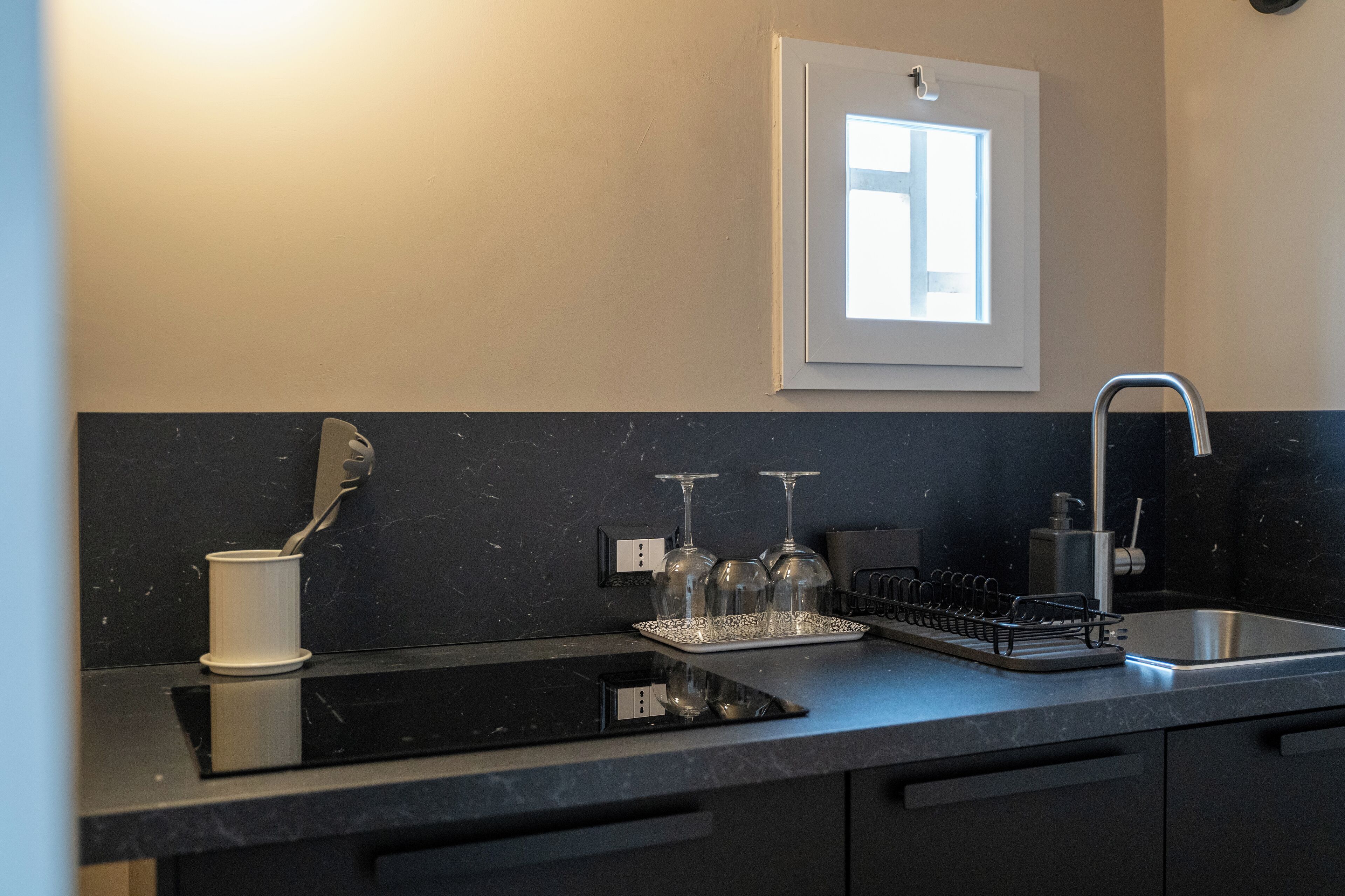 Een moderne keuken met een zwart aanrecht, een ingebouwde oven, een spoelbak en een raam boven de spoelbak.