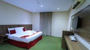 A hotel room with a bed, bedside tables, a desk, a television, and an air conditioning unit. - Golden Aziziyah (Makkah)