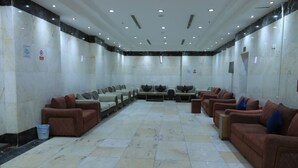 A spacious room with multiple seating areas, including sofas and chairs, arranged in a U-shape. The room has a tiled floor and marble walls. - Golden Aziziyah (Makkah)