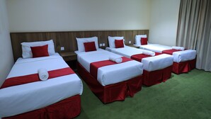 A hotel room with four single beds arranged in a row, each with white bedding and red accents. - Golden Aziziyah (Makkah)