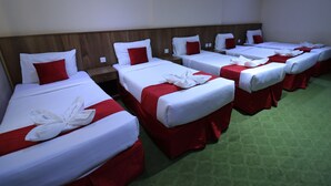 A hotel room with multiple beds, each with white bedding and red accents. - Golden Aziziyah (Makkah)