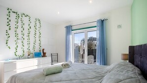 Une chambre à coucher avec un lit, une fenêtre avec des rideaux, un bureau avec une lampe et une vue sur l’extérieur.