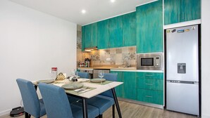 Une cuisine moderne avec des armoires de couleur turquoise, un réfrigérateur en acier inoxydable et un coin repas avec des chaises bleues.