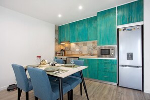 Une cuisine moderne avec des armoires de couleur turquoise, un réfrigérateur en acier inoxydable et un coin repas avec des chaises bleues.