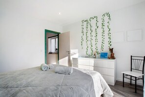 Une chambre à coucher avec un lit, un bureau, une chaise et une plante suspendue.