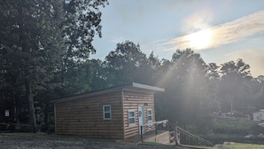 Une petite cabane en bois avec un porche, entourée d’arbres et bordée d’un chemin de gravier.