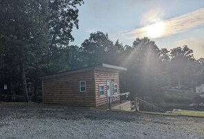 Une petite cabane en bois avec un porche, entourée d’arbres et bordée d’un chemin de gravier.