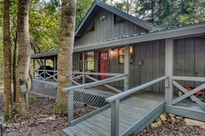 Une cabane dotée d’une terrasse en bois et d’une porte rouge, entourée d’arbres.